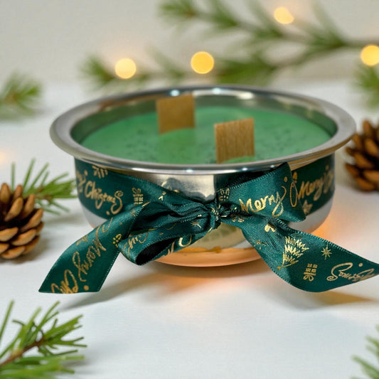 Green candle in a silver holder with a green ribbon, surrounded by pine branches and cones.